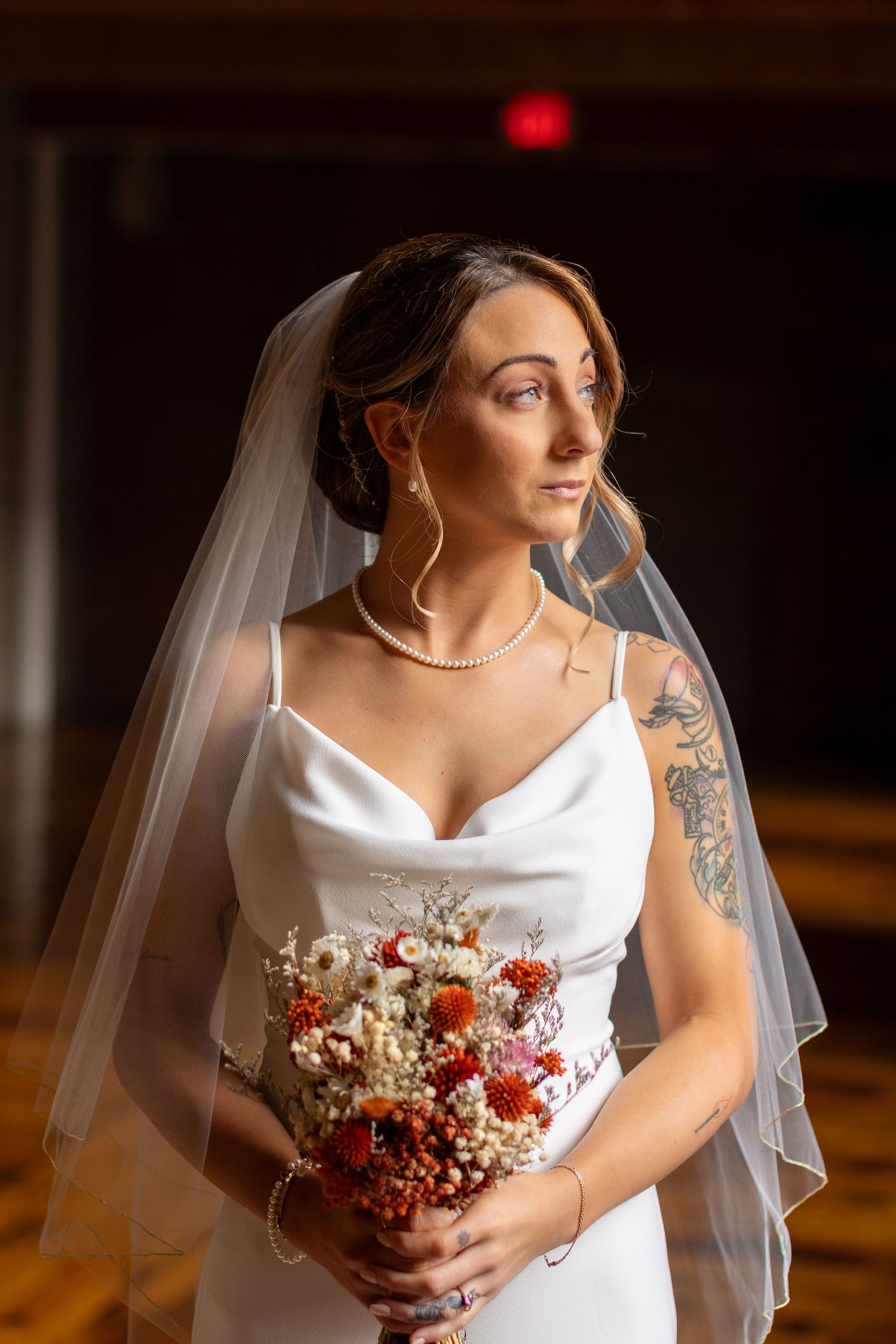 Bride in sleek white gown holding red and white bouquet.