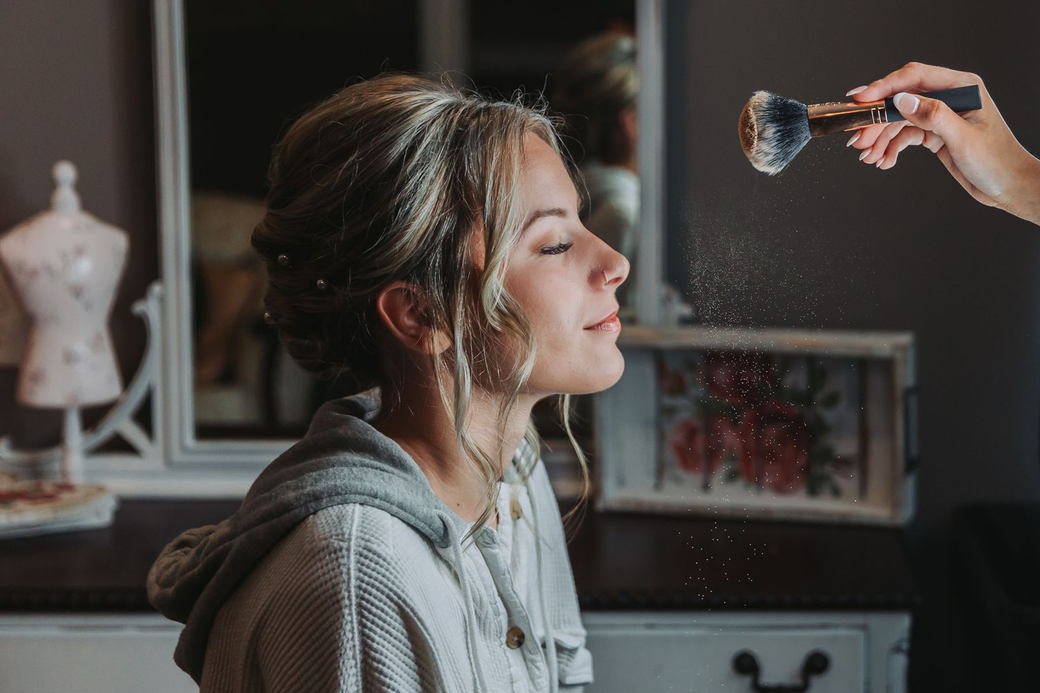 Person getting makeup applied with setting spray in a salon setting.