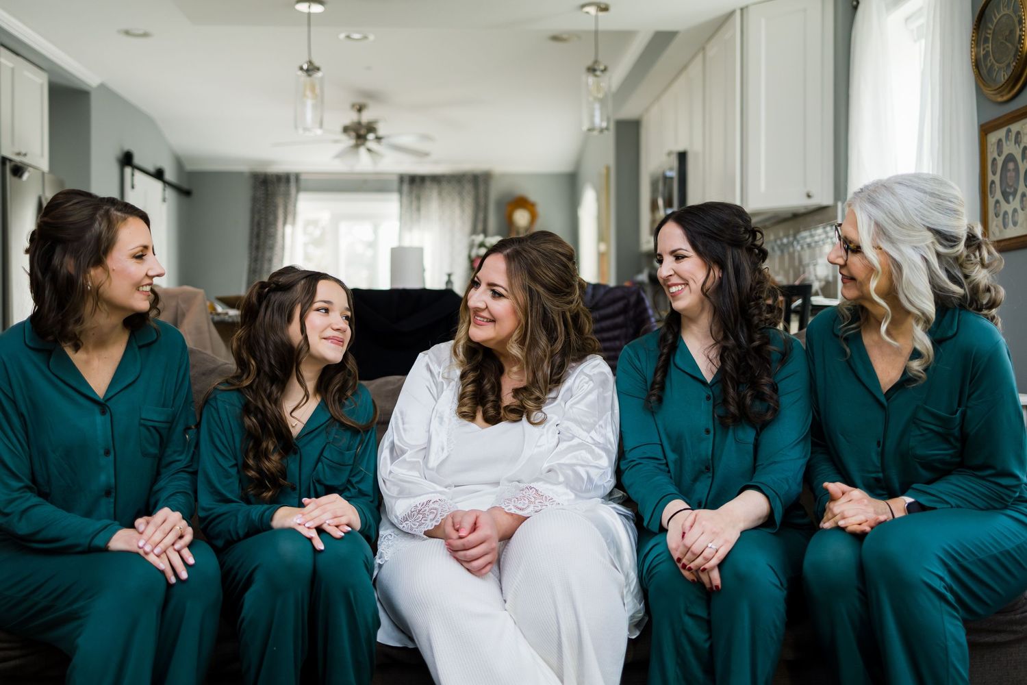 Group in matching teal robes sitting on couch during wedding preparation.