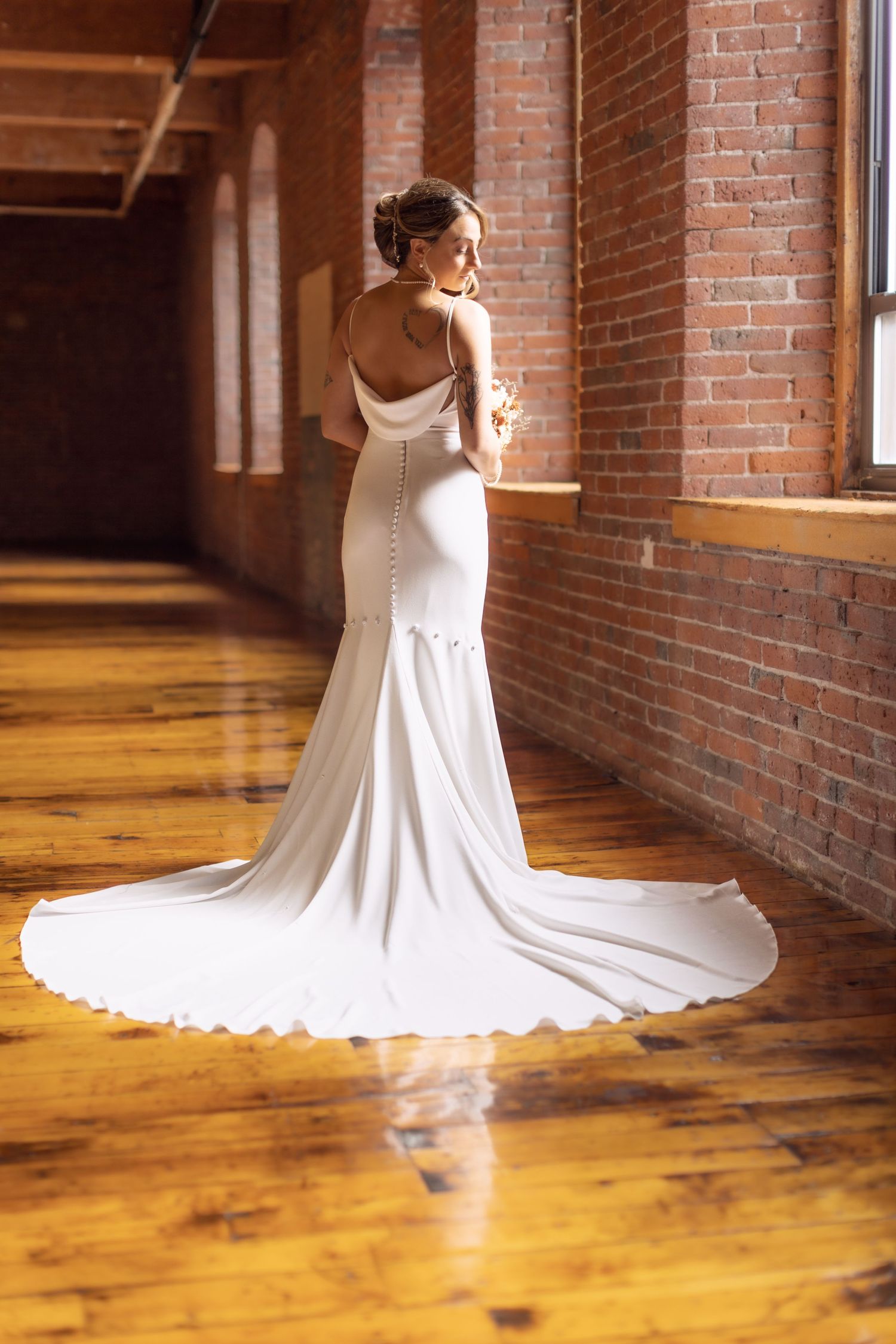 Elegant white wedding gown with train against exposed brick wall.