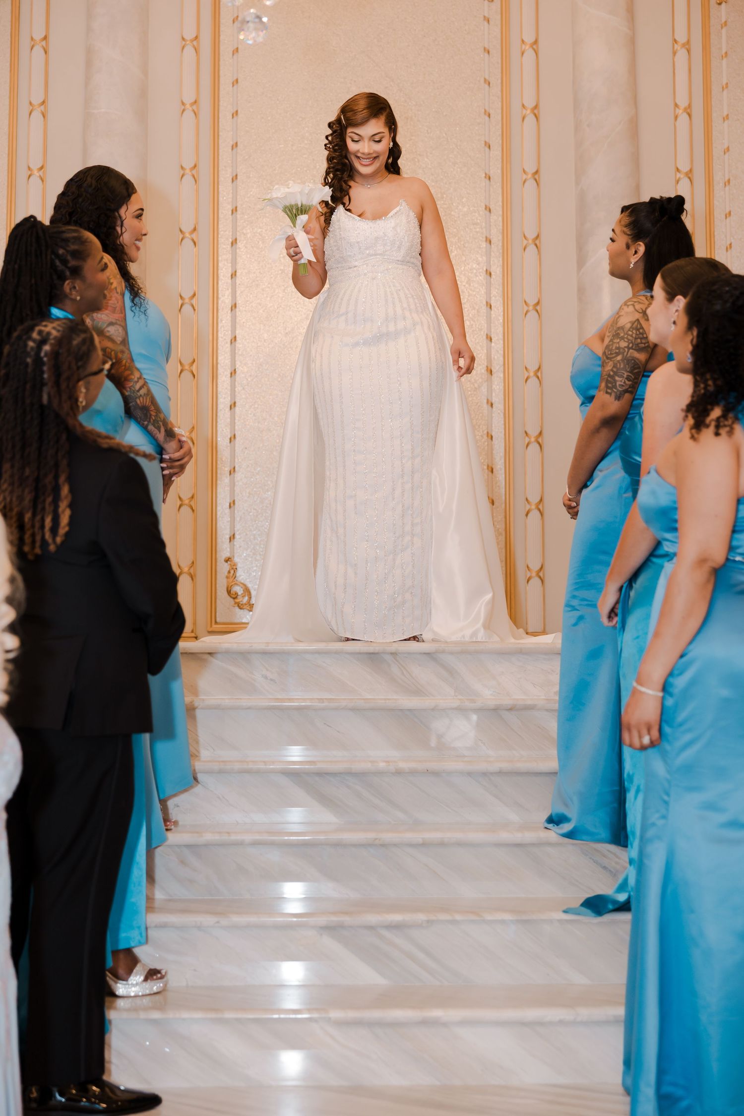 Wedding party members in turquoise dresses and formal attire walk down grand staircase during ceremony.
