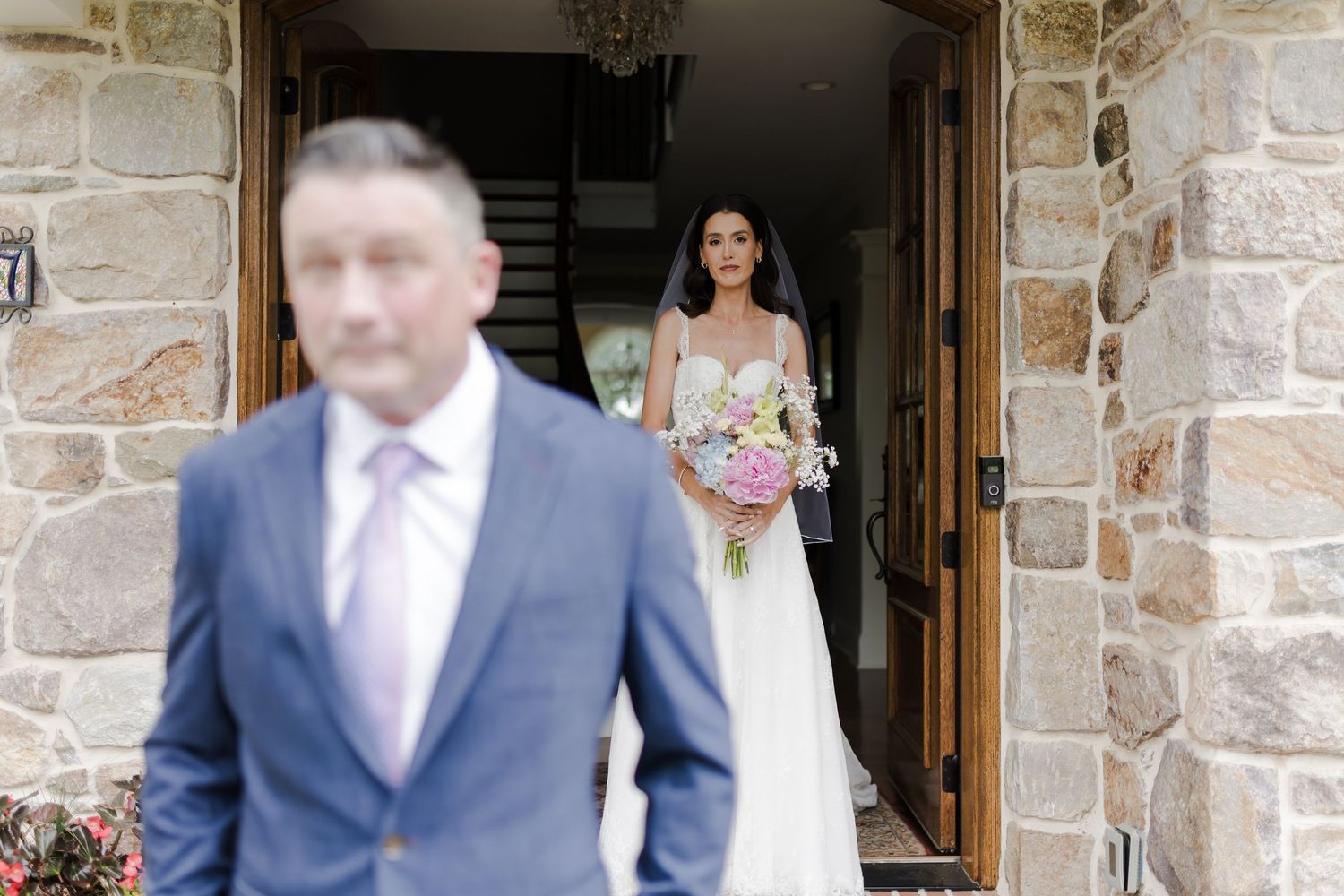 A wedding party stands in front of a rustic stone church entrance adorned with floral decorations.