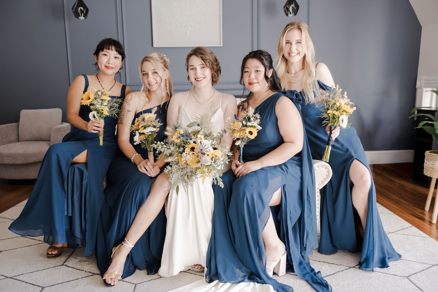 A bridal party in dusty blue bridesmaid dresses and white wedding gown pose together holding sunflower bouquets.