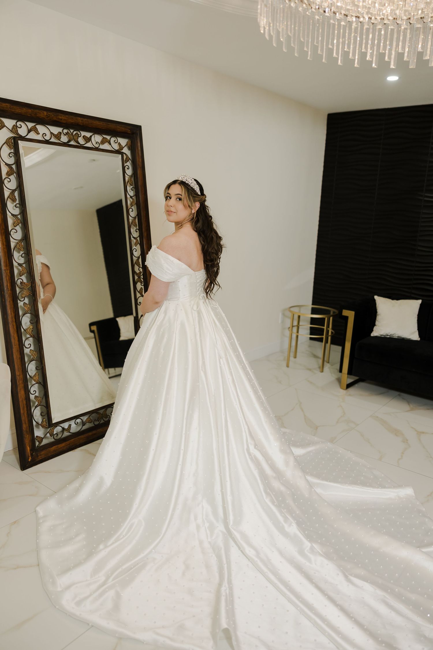 A luxurious white wedding gown with a long flowing train displayed in an elegant room with ornate mirrors.