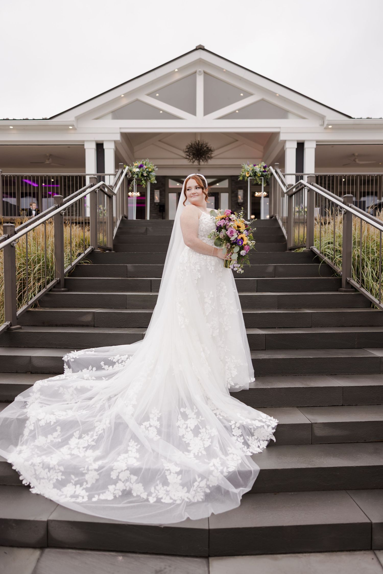A white wedding dress with intricate lace details cascades down outdoor stone steps at a venue.