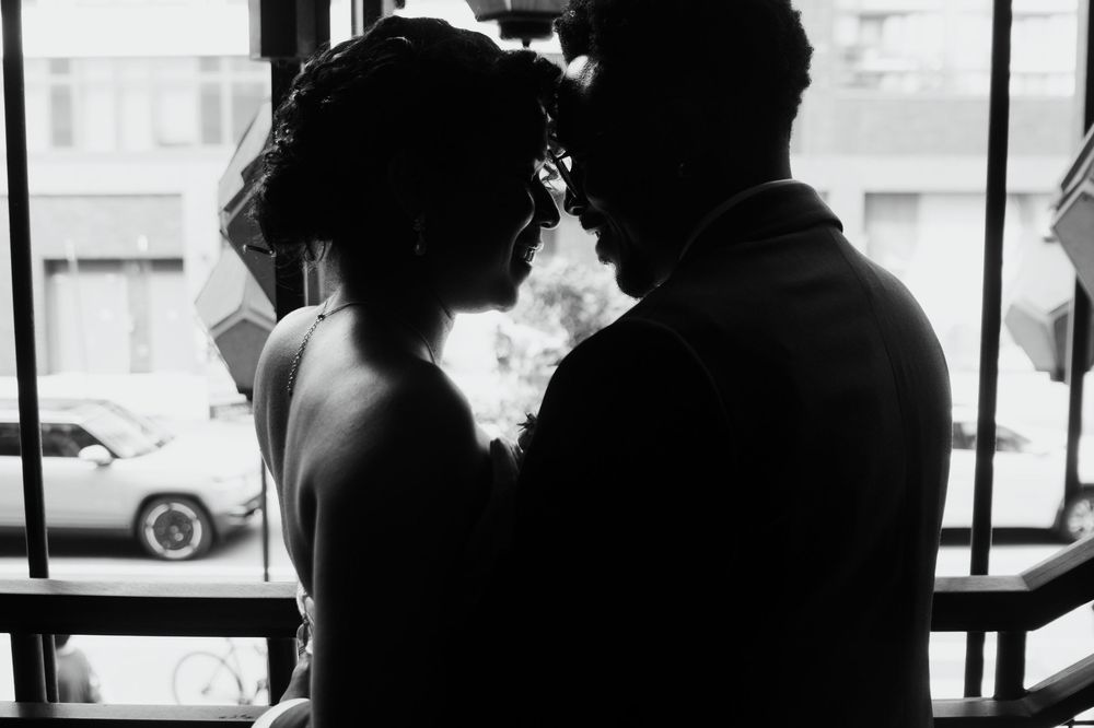 A black and white silhouette of a couple standing by a window with smoke rising between them.