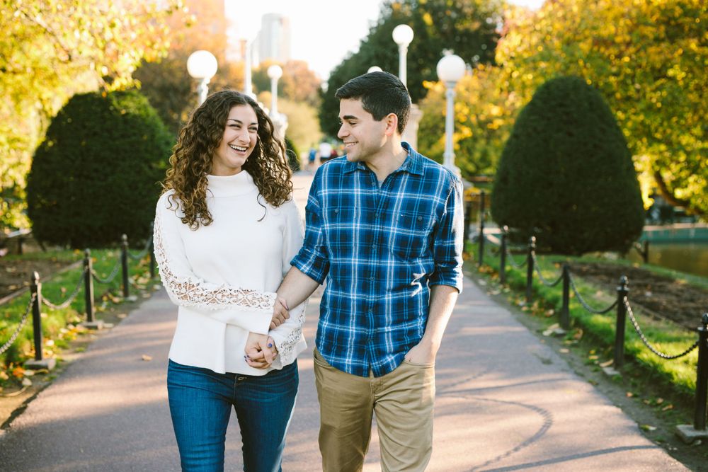 Couple walking together on a path through the Boston Public Garden with ornamental shrubs on an autumn afternoon.