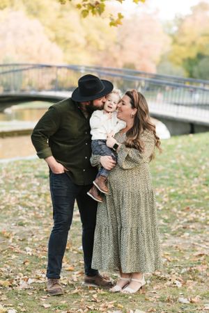 A family sharing a sweet moment near a bridge in an autumn park.