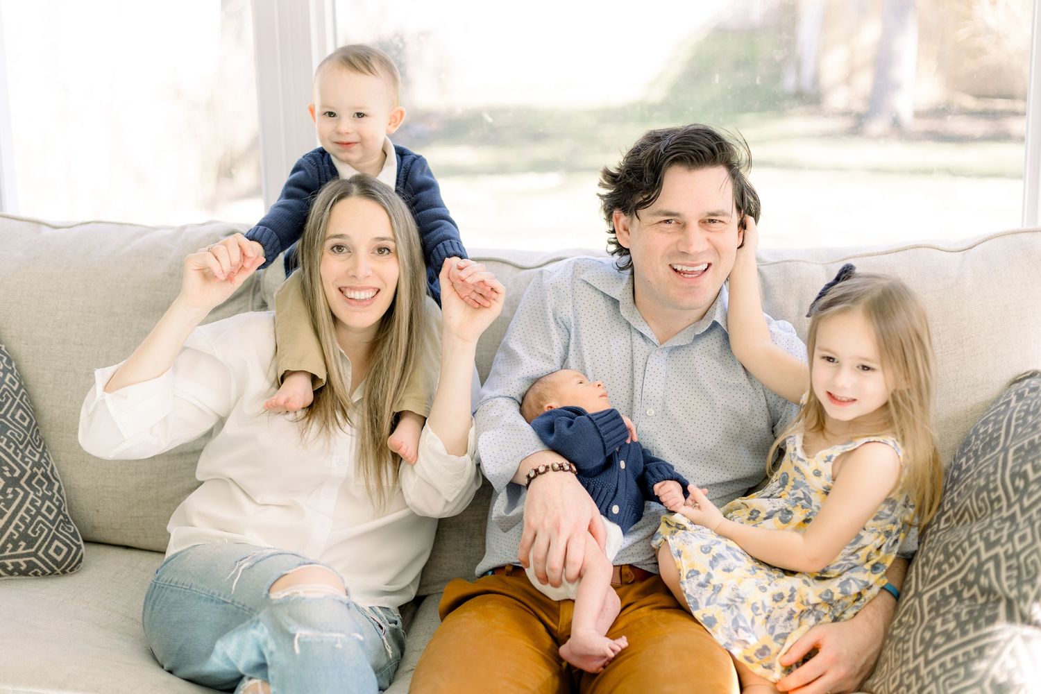 A happy family of four poses together on a cozy beige couch.
