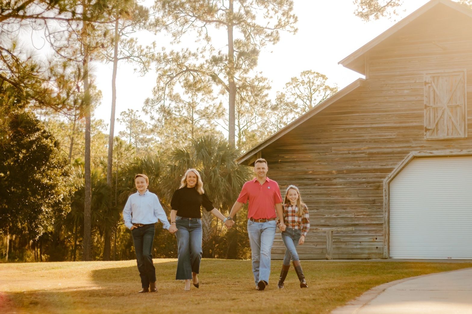 A family walks together on a sunlit path near a rustic barn during golden hour.