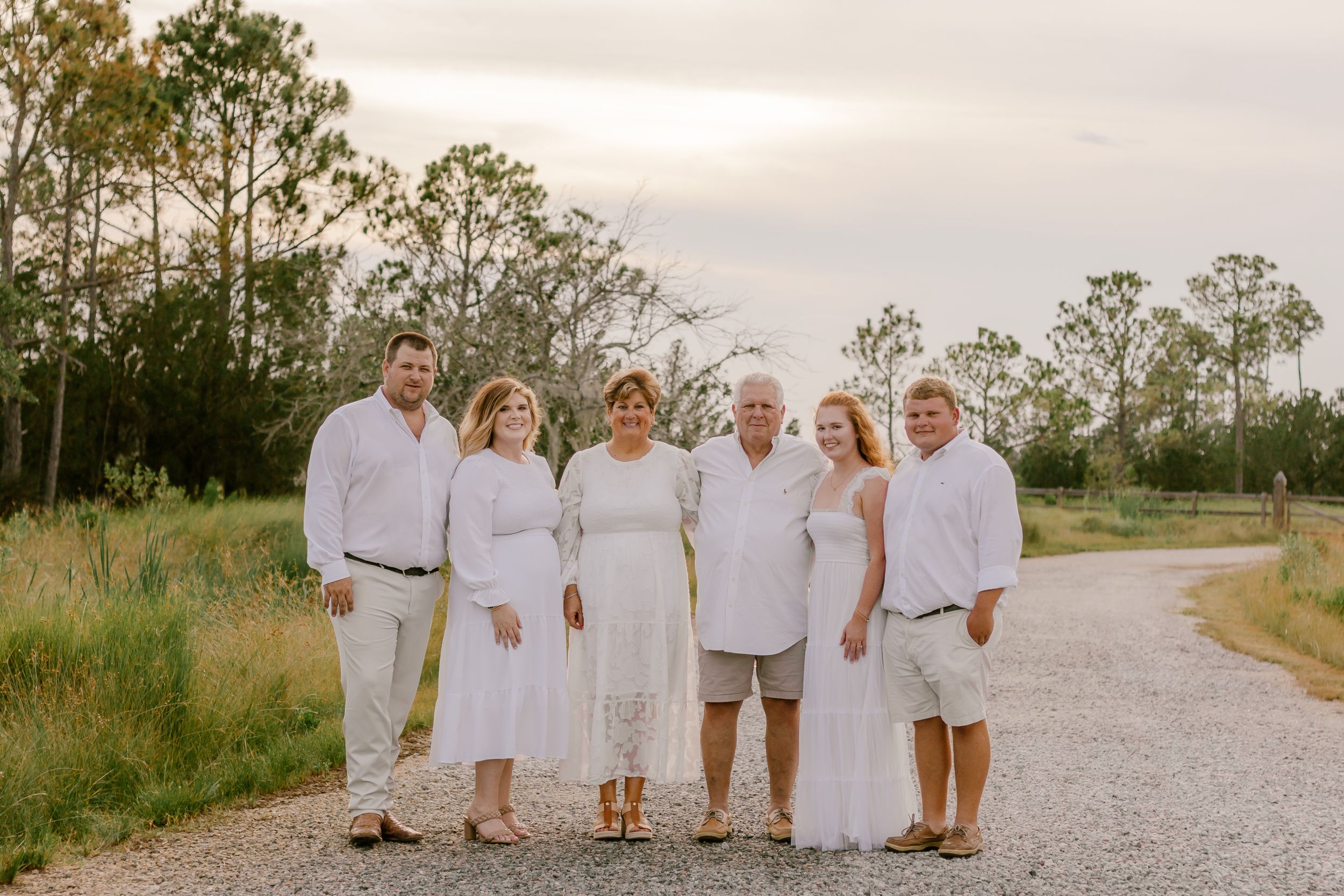 Family in white outfits posed together on gravel path with natural scenery behind.