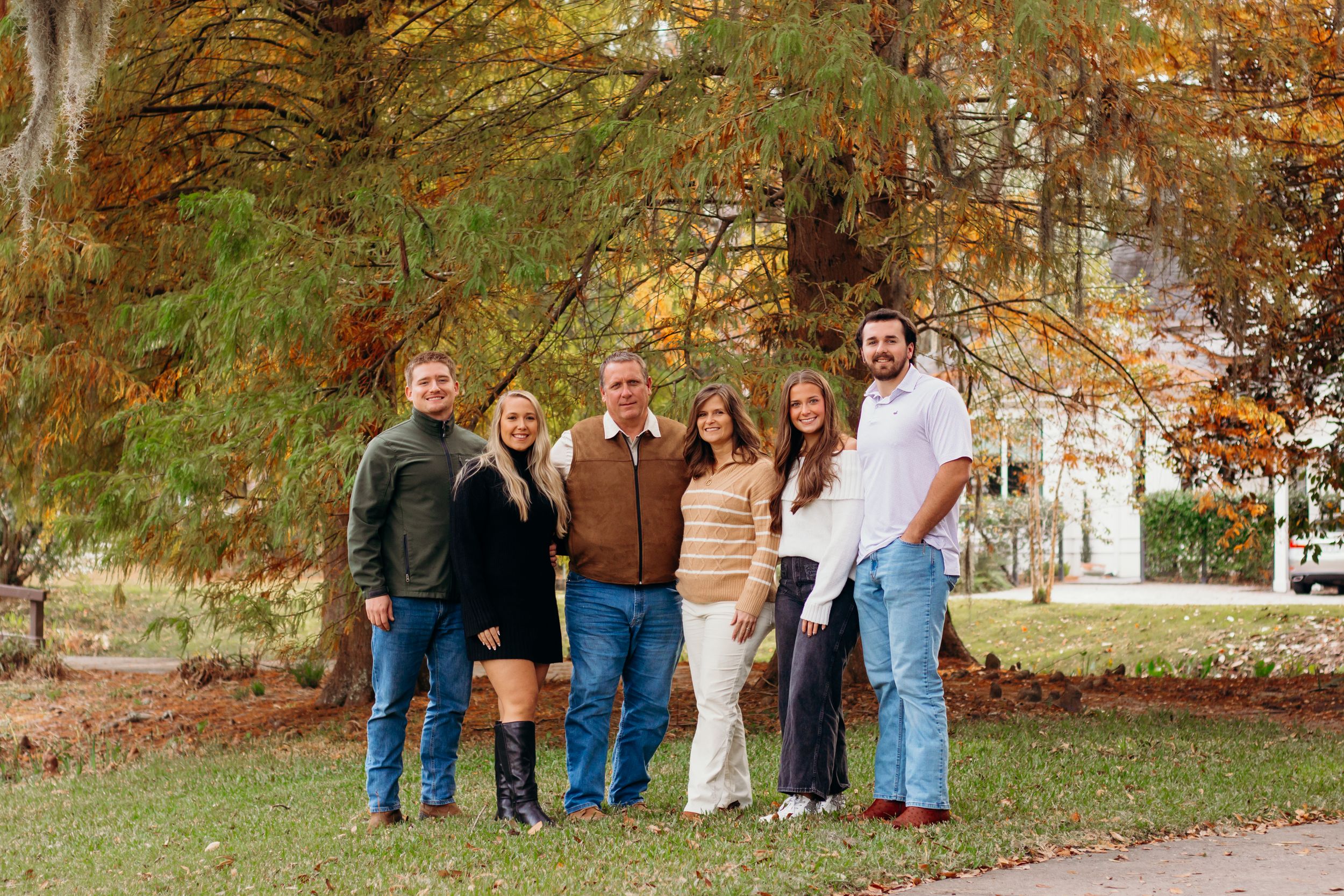 Family standing together on fallen autumn leaves in front of trees with changing colors.
