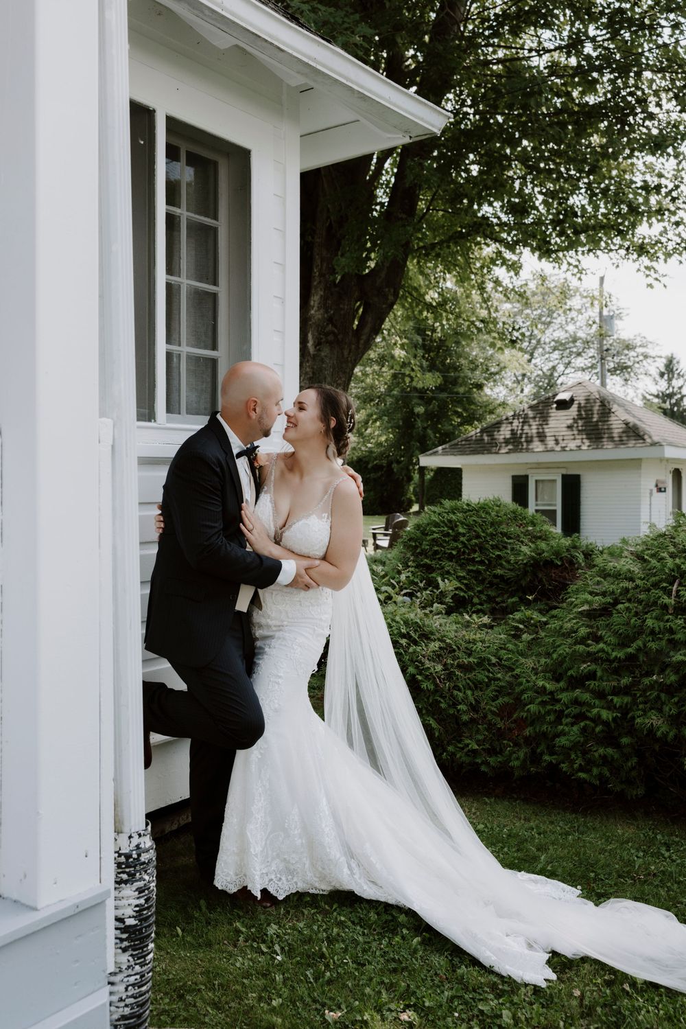 Intimate wedding portrait of couple sharing moment against white house exterior.