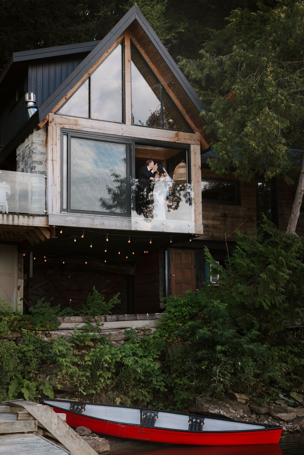 Modern A-frame cabin exterior with glass walls and a red canoe visible in the foreground.