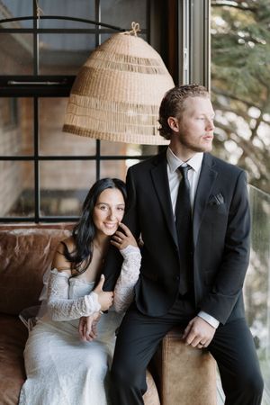 A romantic couple sits together on a brown leather couch beneath woven pendant lights.