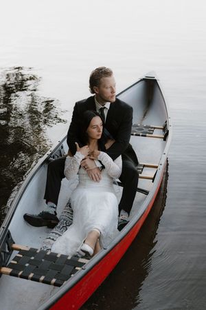 A couple relaxes together in a red and white canoe on calm waters.