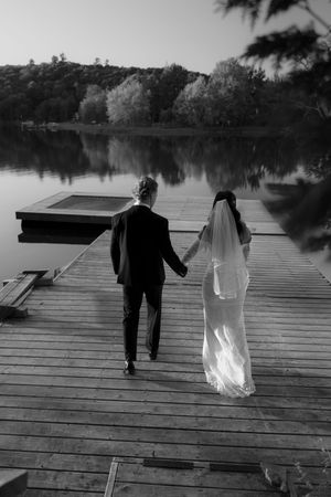 A couple walks along a wooden dock by a peaceful lake.