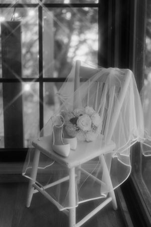 Artistic black and white photo of white dresses hanging in a sunlit window.