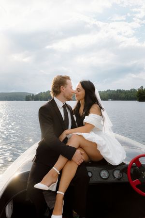 Romantic newlyweds share intimate moments on a boat against a scenic lake backdrop.