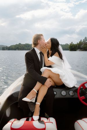 Wedding couple embraces on a speedboat with lake and cloudy sky in background.