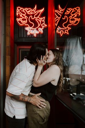 Couple embracing in front of a window with glowing red neon signs.