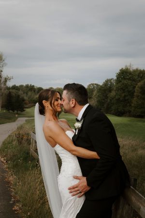 Newlyweds embrace on path with autumn trees in background.