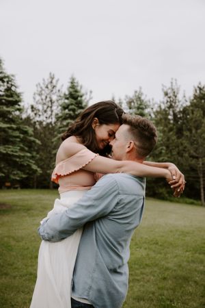 An intimate embrace captured in a natural outdoor setting with pine trees in the background.
