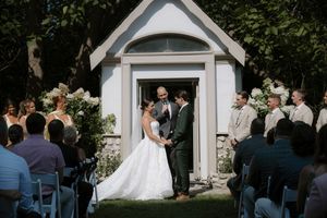 Wedding ceremony taking place at a white chapel with guests in attendance.