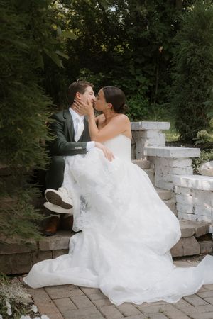 Wedding couple shares intimate moment on white stone steps surrounded by greenery.