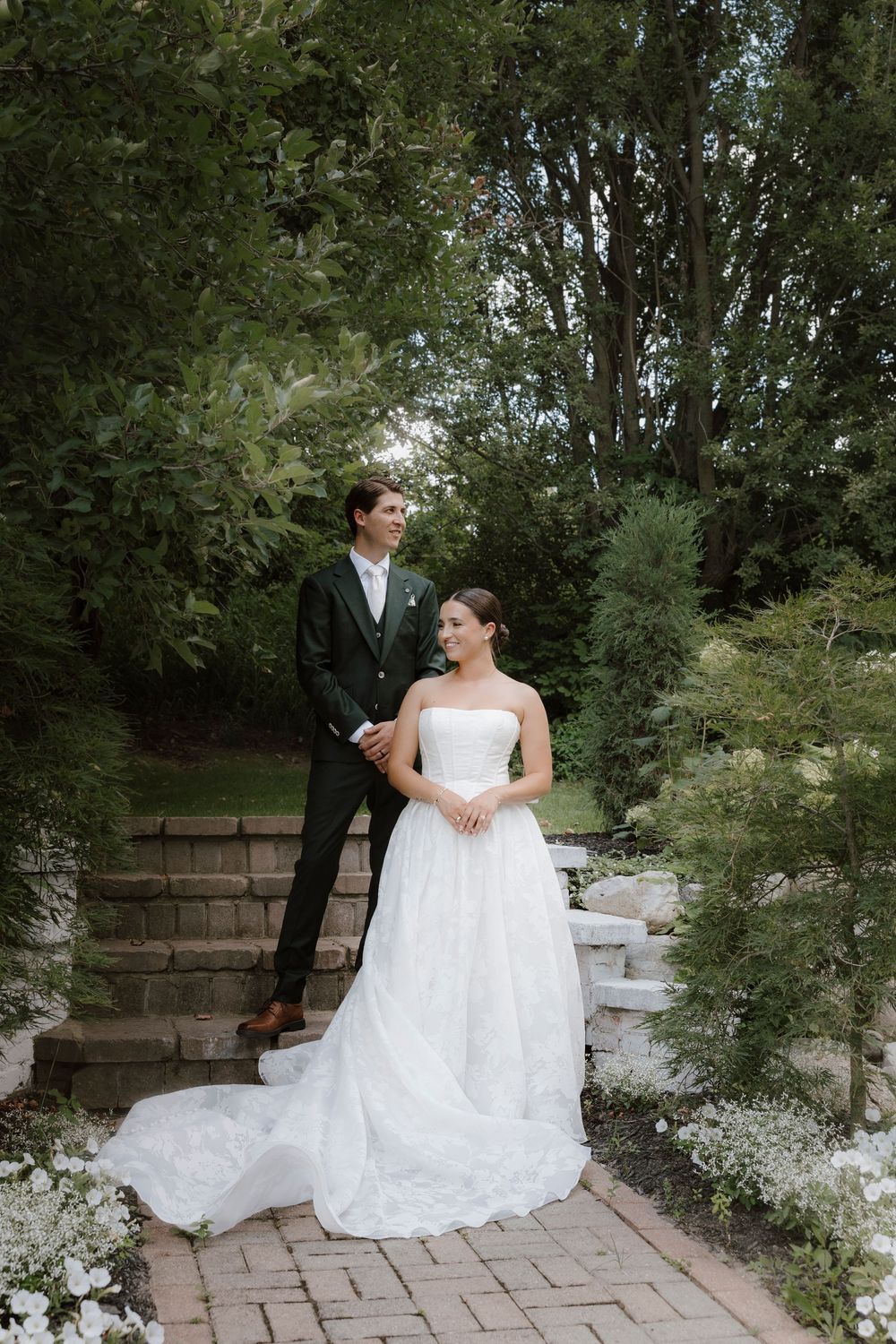 A couple sitting on stone steps in a garden setting during a formal event.