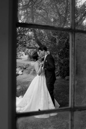 A romantic moment captured through a window frame in a garden setting.
