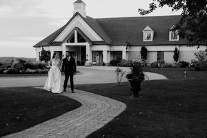 Wedding couple walks along a curved stone path at an elegant outdoor venue at sunset.