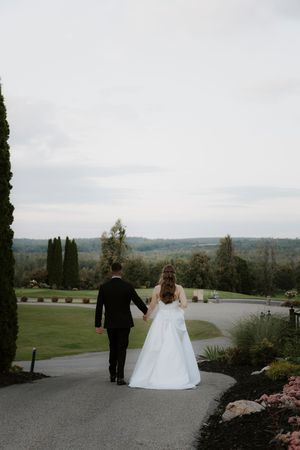 Couple strolls on winding path overlooking scenic mountain views at outdoor wedding venue.