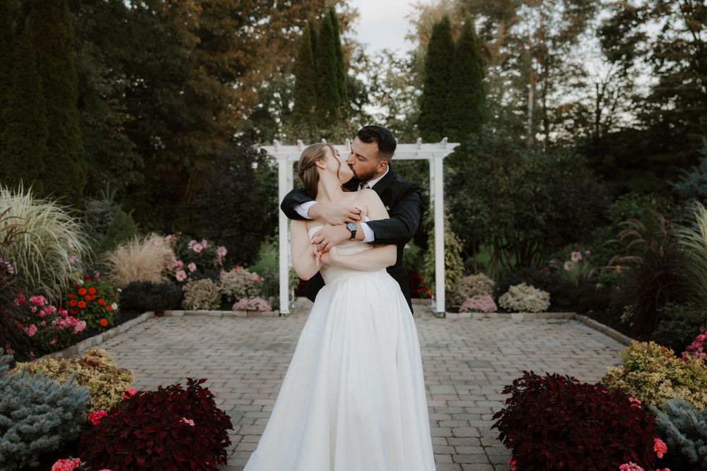 Newlyweds share an intimate moment under a white pergola surrounded by autumn flowers.