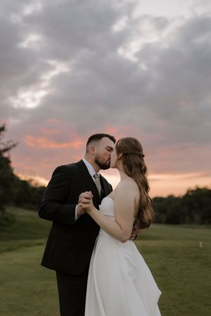 Romantic sunset wedding photos on rolling green hills with dramatic cloudy sky.