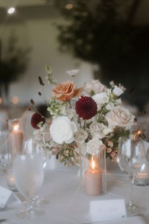 Elegant wedding table decor with blush roses, burgundy dahlias, and glowing candles.
