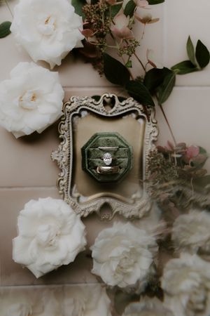 Wedding rings displayed among white roses and vintage decorative elements.