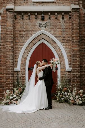 Romantic wedding photos against a brick church with arched red doors.
