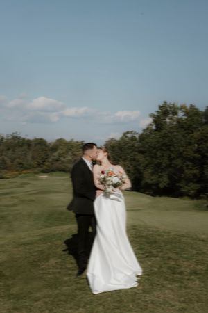Newlyweds embrace on a sunny golf course during their wedding photoshoot.
