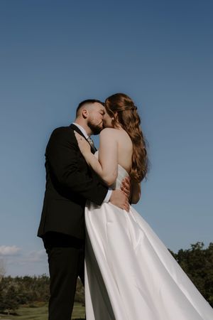 A romantic outdoor wedding photo series showing a couple embracing against a blue sky backdrop.