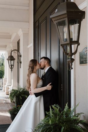 A wedding couple shares tender moments along a covered porch with lantern lighting.