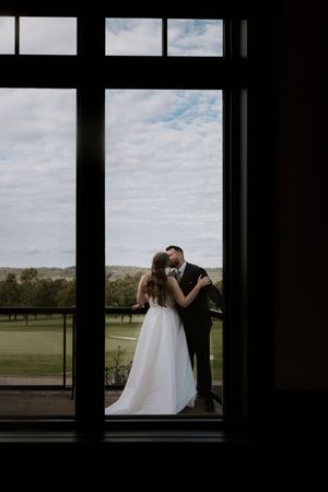 Wedding couple silhouetted through large windows with countryside views.