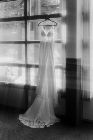 Wedding dress silhouettes hanging in a row against bright windows creating an ethereal black and white effect.