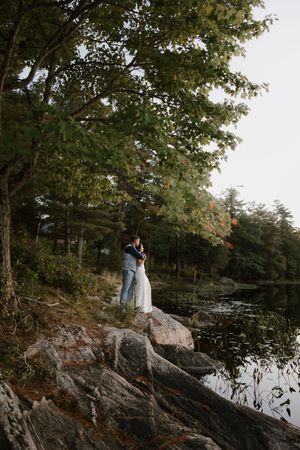 Romantic lakeside portrait on rocky outcrop surrounded by trees during golden hour.