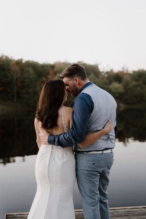 Tender embrace between newlyweds on lakeside dock during sunset.