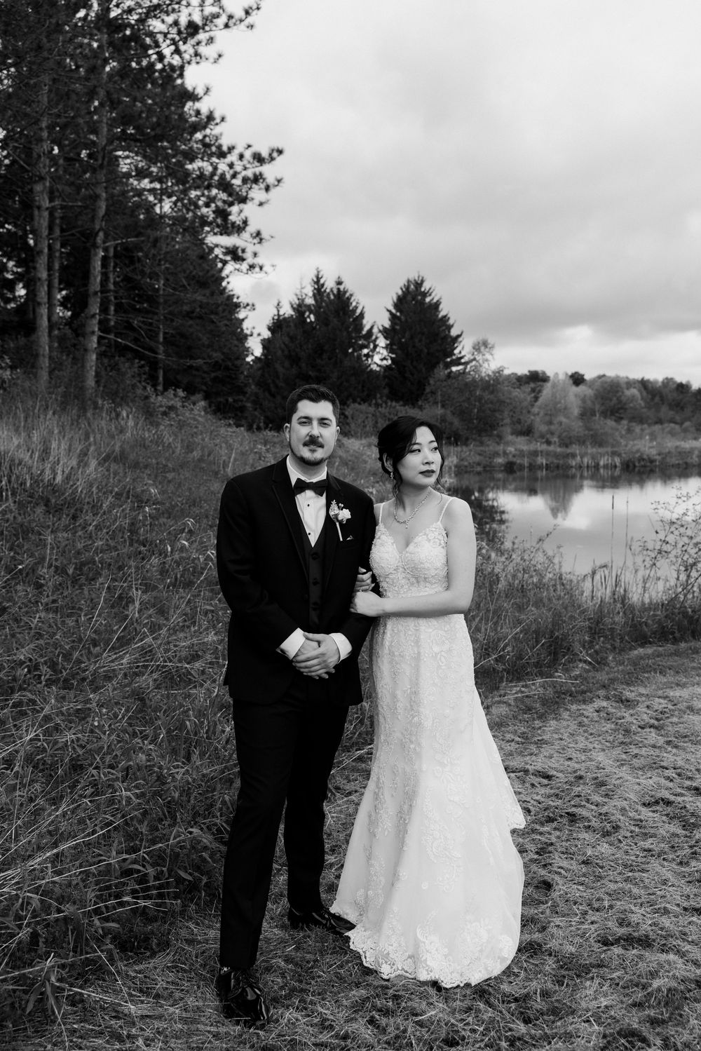 Black and white wedding portraits taken near serene lakeside with natural landscape.