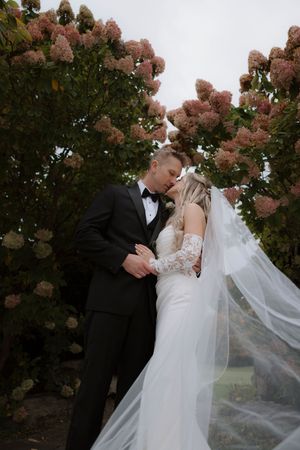 A romantic wedding moment captured under blooming pink hydrangea trees.