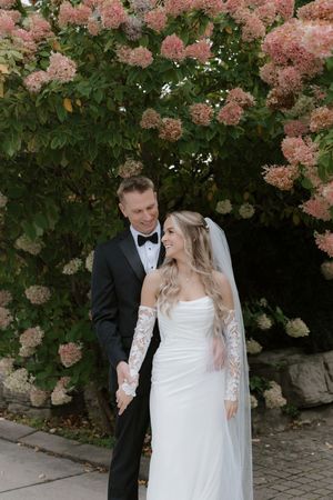 Newlyweds share intimate moments in front of blooming pink hydrangea bushes.