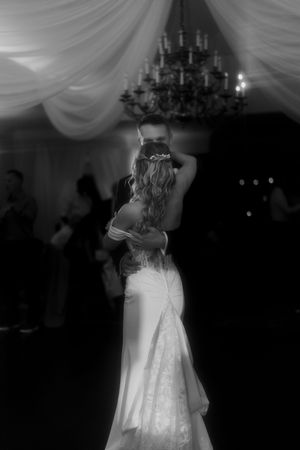 Couple shares a romantic first dance under elegant draped fabric and chandeliers at their wedding reception.