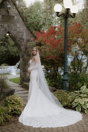 Stunning bridal portrait showcasing a long lace wedding gown and veil against stone architecture and fall foliage.